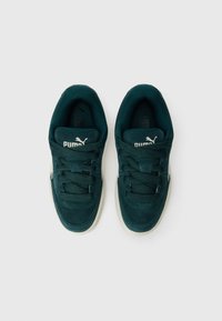 Baskets Puma avec une tige en daim teal foncé, fermeture à lacets, doublure intérieure douce et semelle extérieure en caoutchouc blanche. Présente un logo embossé sur la languette.