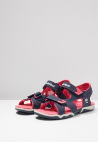 Navy and pink children’s sandals with adjustable straps, cushioned soles, and a textured footbed. Lightweight design suitable for outdoor use.