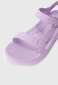 Violetti kumisaapas leveällä hihnalla ja tekstuurilla varustetulla pohjalla. Taipuisa pohja ja sileä viimeistely, jossa on minimaalista yksityiskohtaa.
