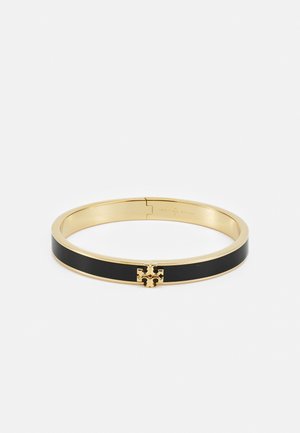 A pulseira de ouro tem um verso em esmalte preto e um emblema decorativo dourado no centro. Textura suave e design elegante.