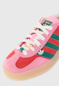 Close-up van een rode en roze Adidas-sneaker met groene strepen, witte veters, decoratieve kralen en een zilveren logocharme aan de zijkant.
