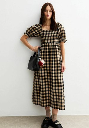 Abito a scacchi nero e beige con corpetto arricciato, maniche a sbuffo e lunghezza midi. Abbinato a una borsa nera con dettagli pompon e mocassini.