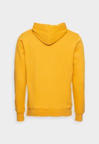 La felpa gialla presenta un tessuto morbido, maniche lunghe e una tasca a marsupio. Sul retro include un cappuccio con coulisse e polsini a costine.