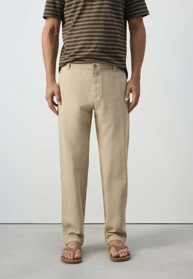 Homme portant un pantalon droit beige associé à des tongs marron et une chemise marron à rayures manches courtes.