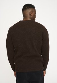 Brun ribbad tröja med rund halsringning och långa ärmar. Mjuk textur och slimmad passform. Synliga sömmar längs ryggen.