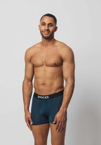 Blaue Boxershorts mit einem schwarzen elastischen Bund, der den Markennamen "SNOCKS" trägt. Der Stoff ist glatt und enganliegend. Das Modell steht mit einem neutralen Ausdruck.