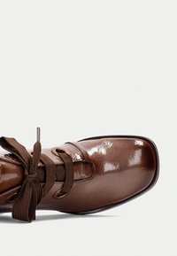 Scarpe in pelle marrone con finitura lucida, punta arrotondata e design con lacci. Presentano occhielli robusti e lacci intrecciati.