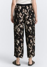 Pantalones de pierna ancha negros con un patrón abstracto en beige y marrón, cinturilla elástica y textura de tela suave. Se llevan con sandalias negras.