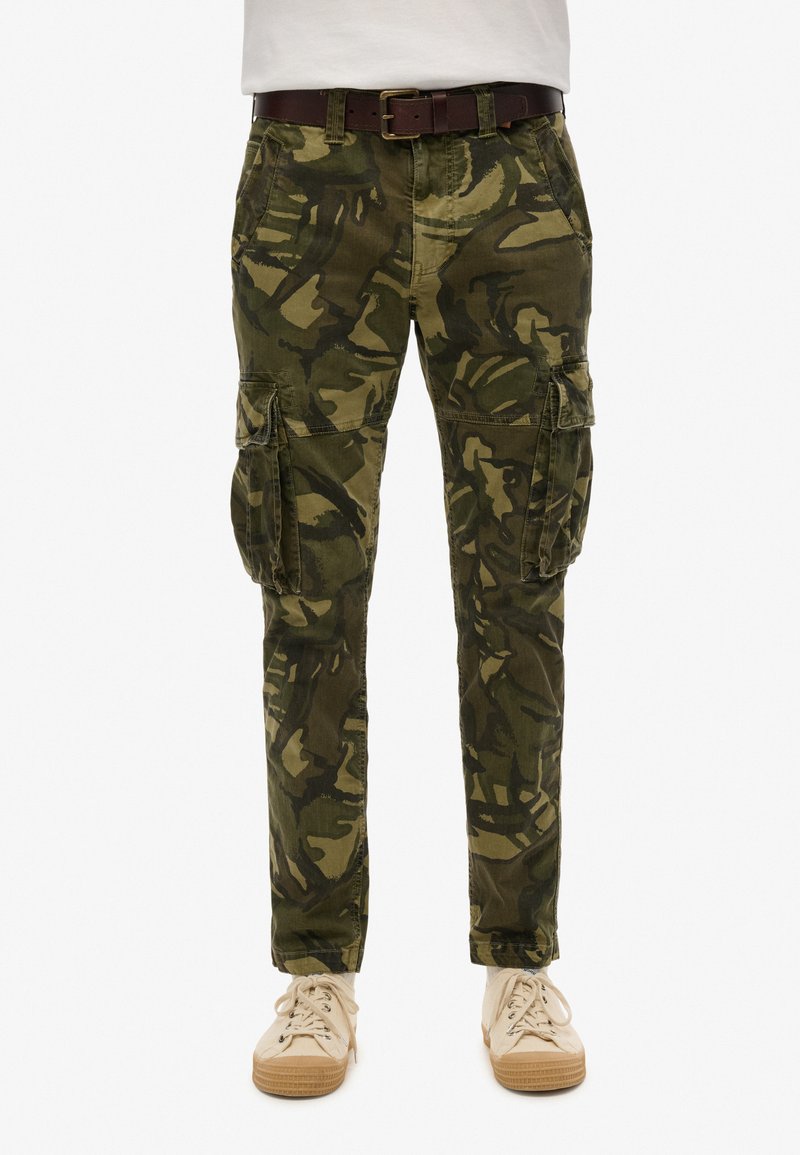 Cargo pants in een groene camouflageprint, gemaakt van duurzaam materiaal, hebben zijzakken en een slanke pasvorm. Draag ze met een bruine riem en lichte sneakers.
