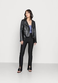 Jaqueta de motoqueiro preta em couro com ferragens prateadas, sobre uma blusa roxa e calças pretas com fendas até as coxas. Sandálias pretas.