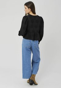 Blouse noire texturée avec manches bouffantes et taille à basque, associée à un jean denim bleu clair à jambes larges et des bottines marron à talons.