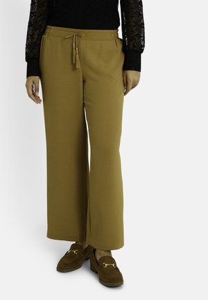 Pantalones de pierna ancha en verde oliva, con un tejido texturizado, cinturilla con cordón y borlas, complementados con mocasines marrones.