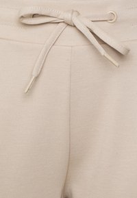 Beige Jogginghose aus strukturiertem Stoff, mit einem Kordelzugbund mit metallischen Enden und kontrastierenden Nähten.