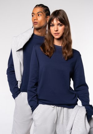 Hemd mit langen Ärmeln in Marineblau aus Baumwollgemisch, kombiniert mit hellgrauen Jogginghosen, die einen lockeren Schnitt und minimalistische Designelemente aufweisen.