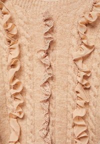 Maglione lavorato a maglia di un rosa chiaro, con tessuto texturizzato e dettagli in pizzo e volant lungo il davanti, creando un effetto visivo a strati.