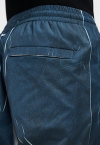 Μπλε σορτς με σχέδιο, κατασκευασμένα από ελαφρύ ύφασμα, με ελαστική μέση και πίσω τσέπη. Διακριτικές λευκές λεπτομέρειες κατά μήκος των ραφών.