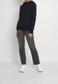 Sudadera navy con puntos blancos y un patrón texturizado, que presenta una capucha con cordones y puños acanalados, combinada con jeans rectos grises y zapatillas blancas.