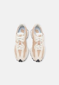 Paire de baskets New Balance beige et blanches avec lacets blancs et semelles intérieures bleu clair, vue de dessus sur fond blanc.