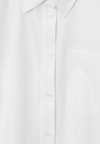 White button-up shirt with a classic collar, long sleeves, a chest pocket, and smooth fabric texture. Features clear plastic buttons.