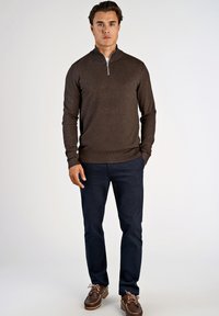 Sweater castanho com fecho, de design ajustado, usado com calças azuis-marinho e sapatos castanhos. Textura suave com punhos e bainha canelados.