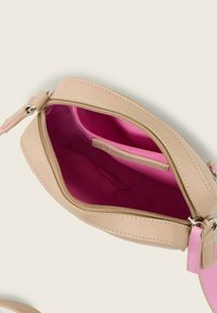 Bolso de cuero beig con cremallera y correa en rosa; el interior cuenta con un revestimiento rosa brillante y un pequeño bolsillo. Cierre de cremallera y detalles de costura visibles.