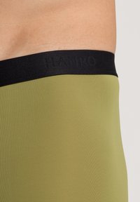 Prenda ajustada de color verde caqui con una cinturilla elástica negra en la que aparece el nombre de la marca en relieve. Textura suave, diseño sin costuras.