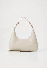 Smėlinės odos petnešinė rankinė su išlenkta silueto forma, reguliuojamu dirželiu ir subtiliais logotipo detalėmis priekyje. Lygi tekstūra.