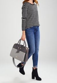 Sac à main gris et noir avec double poignée et bandoulière amovible ; femme portant un haut rayé, un jean bleu et des bottines noires.