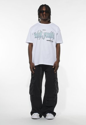 White cotton t-shirt with blue graphic text "lol(s)t, you(th)" and black cargo pants. Model wearing sunglasses and white sneakers.