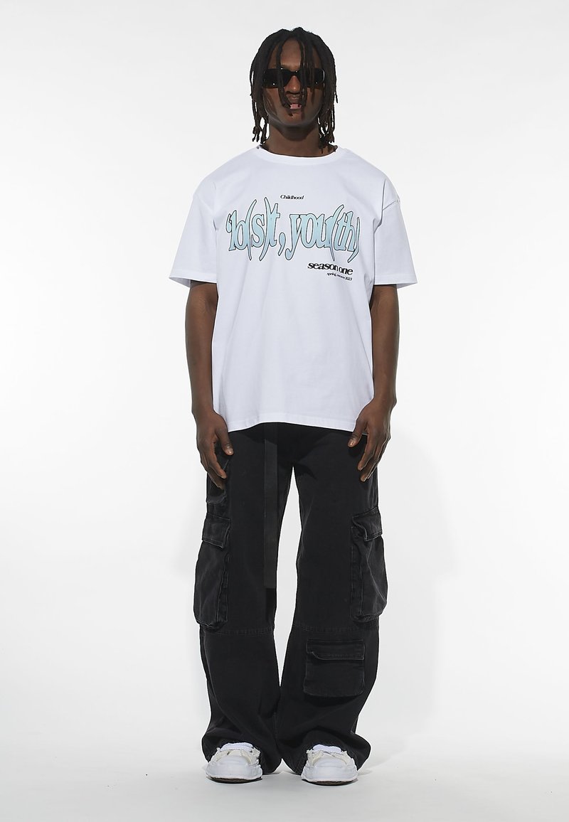 White cotton t-shirt with blue graphic text "lol(s)t, you(th)" and black cargo pants. Model wearing sunglasses and white sneakers.
