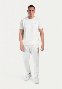 Weißes Baumwoll-T-Shirt und passende Jogginghose. Weiche Textur, Rundhalsausschnitt, kurze Ärmel, minimales Logodetail. Kombiniert mit weißen Turnschuhen.