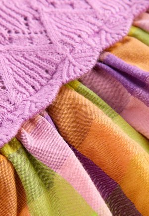 Bodice tricoté violet avec des motifs complexes au-dessus d'un tissu multicolore présentant une texture à carreaux orange, verte et violette.