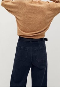 Maglione marrone a maglia con vestibilità comoda, abbinato a pantaloni in denim blu scuro a vita alta con due tasche posteriori.