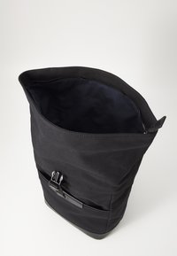 Bolsa de tela negra con un diseño estructurado, abertura amplia y un interior con cremallera, que cuenta con un bolsillo lateral y un cierre de hebilla negra.