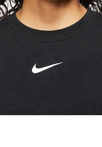 Svart bomulls-T-shirt med rund halsringning och en vit Nike-logotyp på framsidan, visas utan någon ytterligare kontext eller bakgrund.