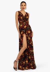 Maxi-Kleid mit floralem Muster auf schwarzem Hintergrund, gelben und roten Blumenmustern, V-Ausschnitt, geraffter Taille und Schlitz vorne. Styliert mit Riemchen-Heels.