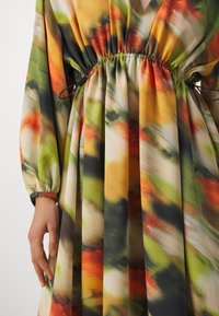 Robe à manches longues avec taille à cordon élastique, présentant un motif abstrait multicolore aux tons verts, orange, jaune, gris et beige.
