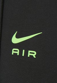 Nike Air-logotypen på svart tyg. Logotypen har en grön swoosh ovanför ordet "AIR" i fet, ren typografi. Mjuk textur.