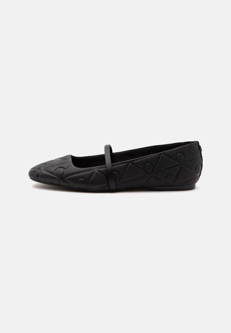 Chaussure plate noire avec un bout arrondi, un motif géométrique embossé et une fine bride unique sur le dessus, vue de profil.
