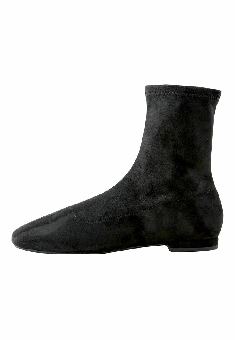 Bottine en daim noir avec semelle plate et bout arrondi, présentant un design lisse et ajusté avec des détails de couture subtils.