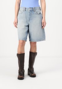 Svetlo modri denim kratki hlače s klasičnim krojem, z gumbnim pasom, štirimi žepi in zvitimi robovi, v kombinaciji s svetlomodrimi čevlji do kolen.