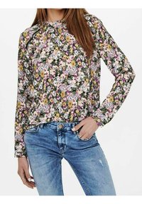 Blumenbluse in Schwarz, Lila und Gelb, mit langen Ärmeln und gerafftem Ausschnitt, kombiniert mit hellblauen, distressed Jeans.