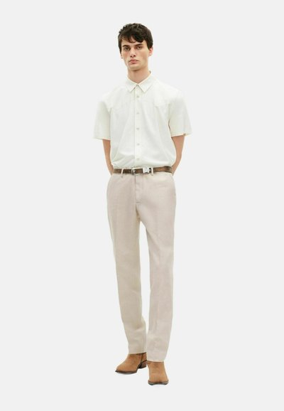 Helles, kurzärmliges Hemd mit Satinfinish, kombiniert mit hellbeigen, taillierten Trousers und tanfarbenen Wildleder-Stiefeletten.