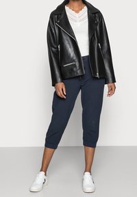 Veste de moto en cuir noir avec fermetures éclair argentées, haut en dentelle blanche et pantalon court bleu marine. Des baskets blanches complètent la tenue.