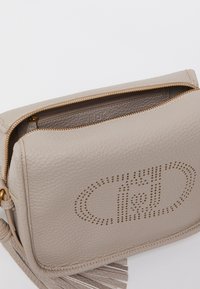 Sac en cuir gris avec fermeture éclair, détail de logo perforé et accent de pompon. Surface texturée et quincaillerie dorée.