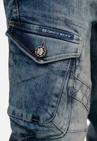 Pantaloni cargo in denim con una tonalità di blu scuro, molteplici tasche, cuciture decorative e un bottone argento con dettagli in rilievo.