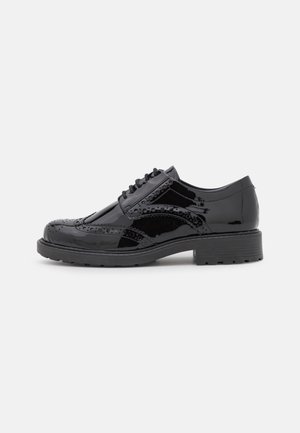 Chaussure brogue en cuir verni noir avec des détails à bout d’aile, bout rond, fermeture à lacets et semelle en caoutchouc épaisse.