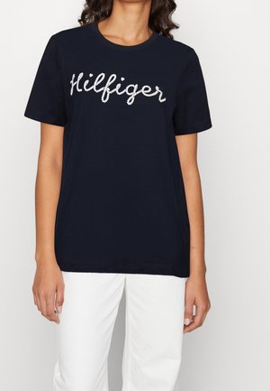 Granatowa koszulka bawełniana z białym logo "Hilfiger" w kursywie, okrągłym dekoltem i krótkimi rękawami. Luźny krój z minimalnym wzornictwem.