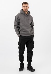 Šedá mikina s kapucí a přední kapsou typu "kangaroo", spárovaná s černými cargo kalhotami se bočními kapsami a černými šněrovacími botami.