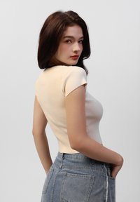 Lys beige, ribbet kortermet topp kombinert med et denimskjørt. Stoffet ser teksturert ut, sitter tett rundt midjen, med en klassisk design.